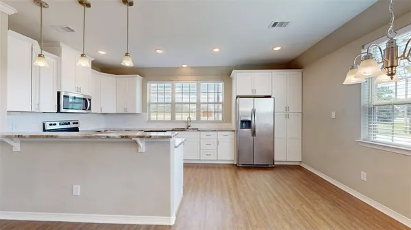 a kitchen with stainless steel appliances granite countertop a refrigerator a sink dishwasher a oven and white cabinets with wooden floor