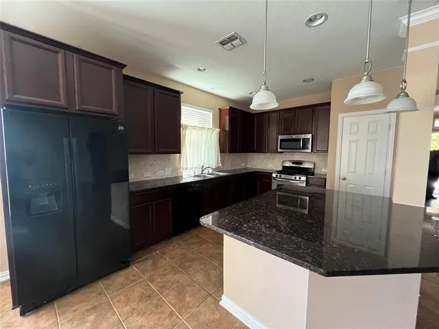 a kitchen with stainless steel appliances granite countertop a refrigerator a sink dishwasher a stove and a refrigerator with wooden cabinets