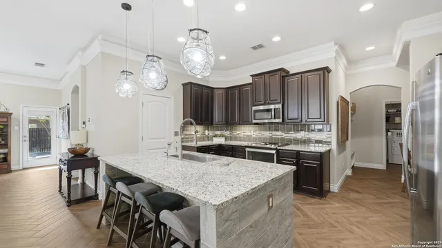 a kitchen with stainless steel appliances granite countertop a stove a refrigerator a kitchen island a sink cabinets and chairs