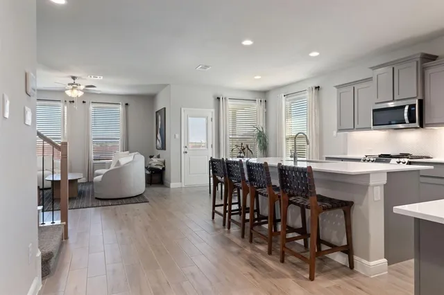 a open kitchen with stainless steel appliances granite countertop a dining table chairs refrigerator and microwave