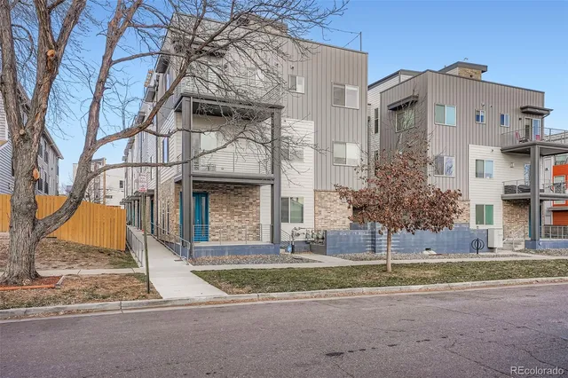 a view of a white house with large windows and a yard with plants