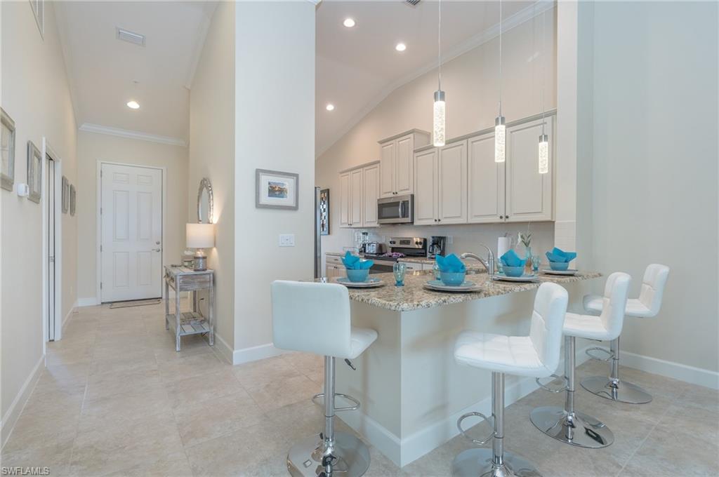 9419 Benvenuto Court, Unit 204 Naples, FL 34119 - Photo 18 of 50 Kitchen with crown molding, a kitchen bar, decorative light fixtures, light stone countertops, and a peninsula