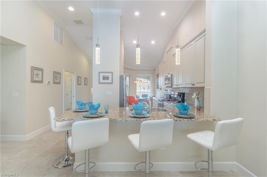 9419 Benvenuto Court, Unit 204 Naples, FL 34119 - Photo 23 of 50 Kitchen featuring a breakfast bar, crown molding, tasteful backsplash, a peninsula, and light stone counters