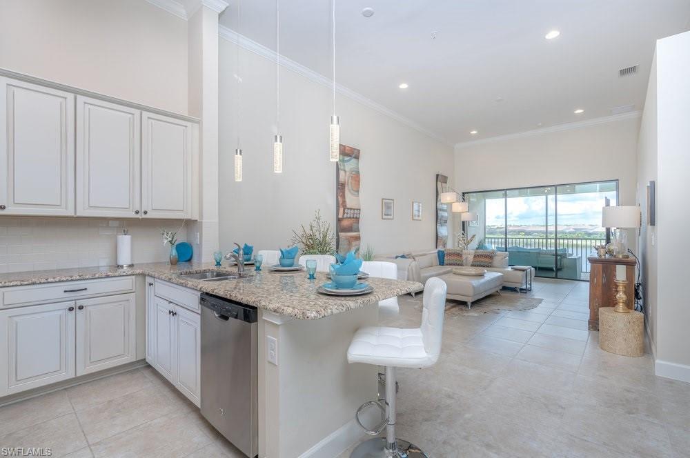 9419 Benvenuto Court, Unit 204 Naples, FL 34119 - Photo 25 of 50 Kitchen featuring backsplash, light stone counters, crown molding, a kitchen bar, and pendant lighting