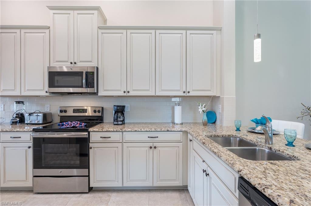 9419 Benvenuto Court, Unit 204 Naples, FL 34119 - Photo 27 of 50 Kitchen with stainless steel appliances, light stone countertops, decorative backsplash, and white cabinetry