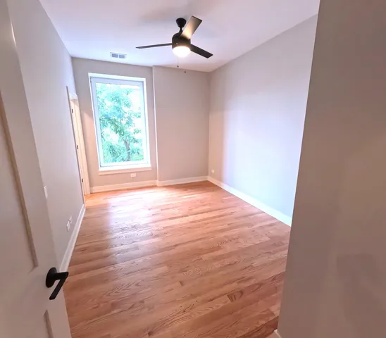 an empty room with wooden floor ceiling fan and window