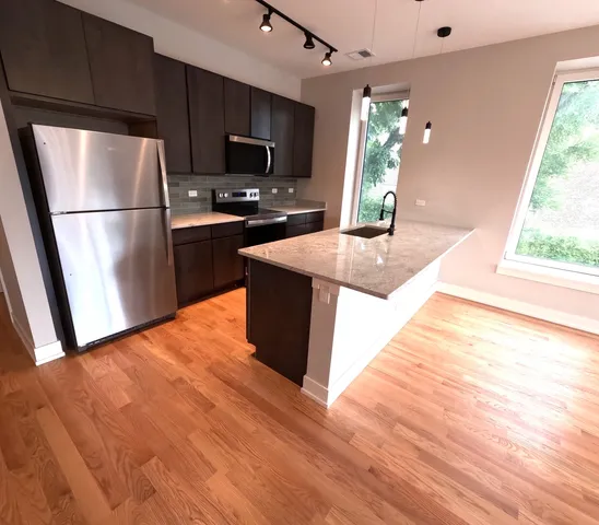 a kitchen with stainless steel appliances granite countertop a refrigerator a stove a sink and a wooden floors