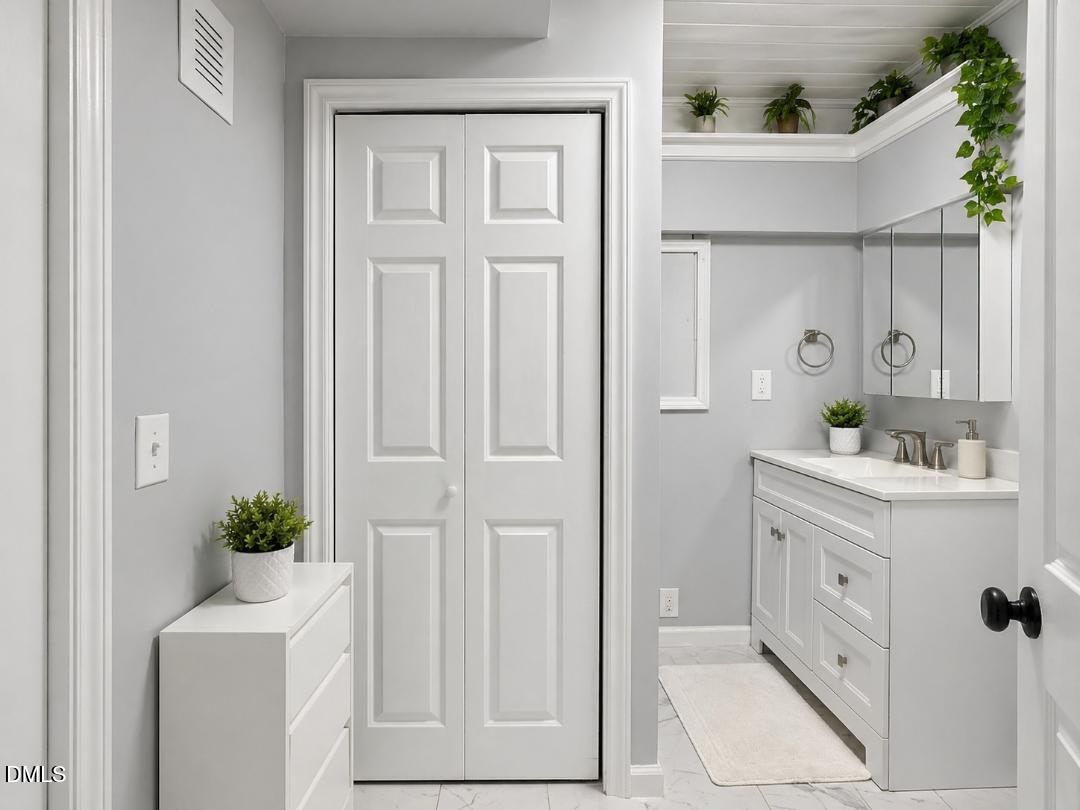 1204 Belhaven Road Cary, NC 27513 - Photo 12 of 32 White paneled bi-fold doors, white bathroom vanity with integrated sink, brushed nickel faucet, wall-mounted medicine cabinet, and marble-look flooring