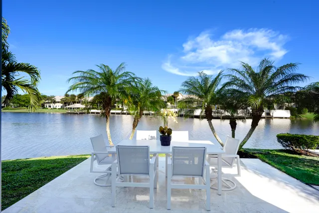 a view of a lake with table and chairs potted plants and palm trees