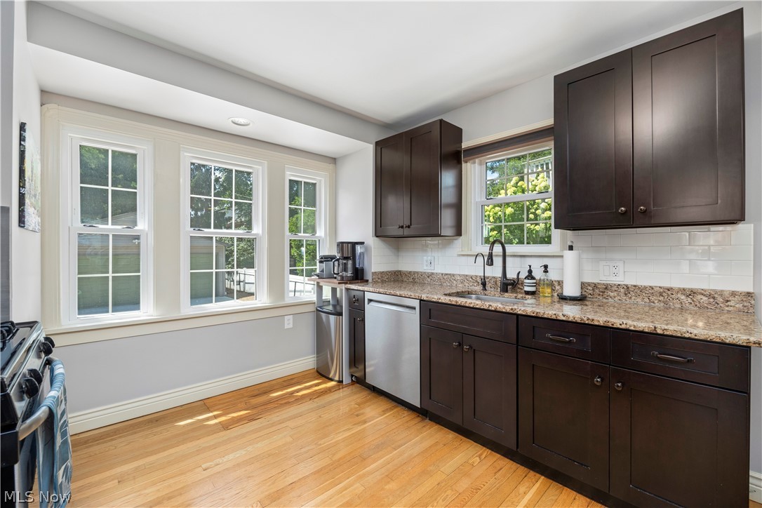 26019 Lake Road Bay Village, OH 44140 - Photo 11 of 40 Hardwood flooring extends throughout this kitchen featuring dark wood cabinetry, granite countertops, stainless steel appliances, and a white subway tile backsplash