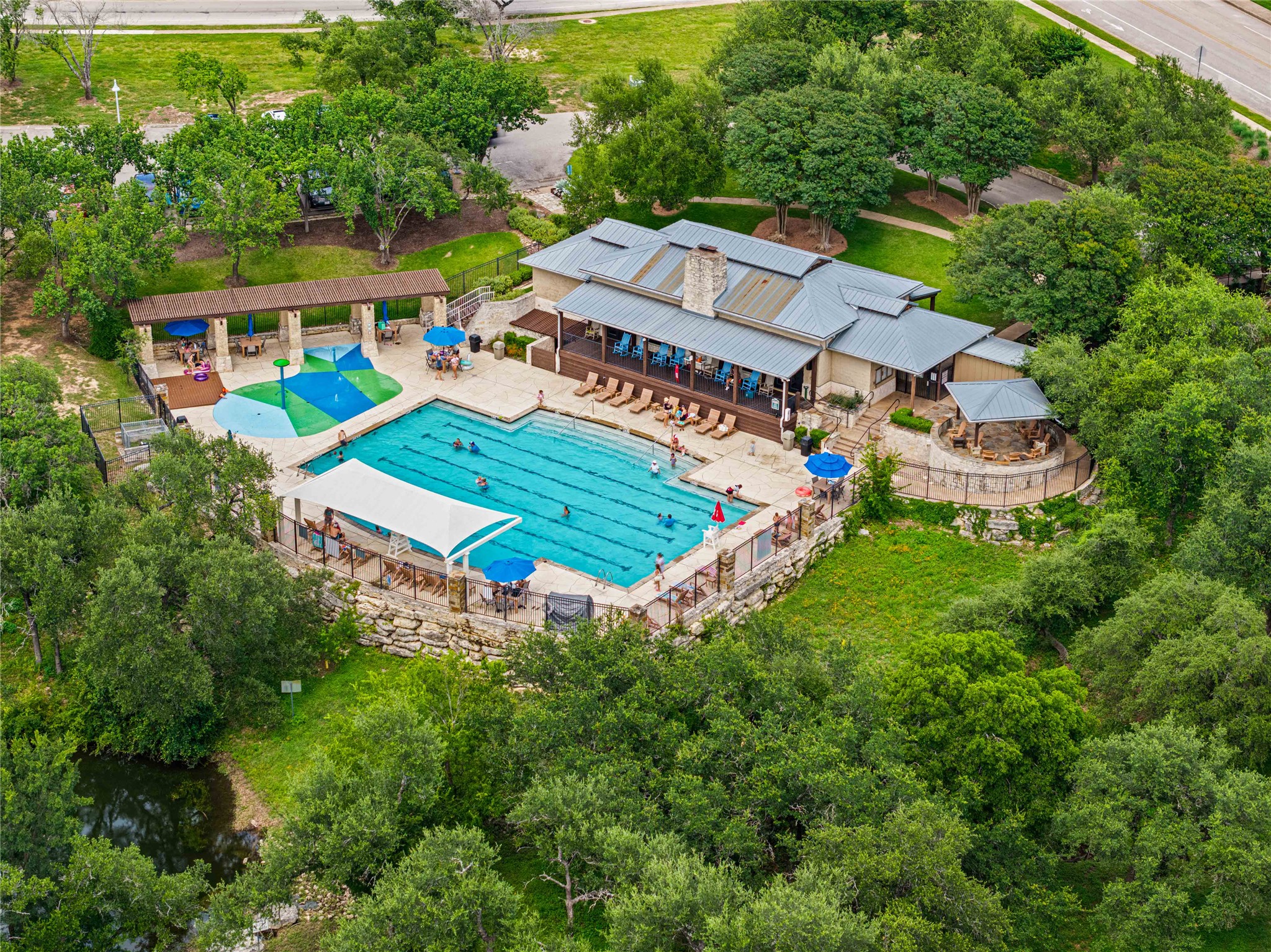 10700 Pointe View Drive Austin, TX 78738 - Photo 32 of 35 An aerial perspective reveals a vibrant community pool area nestled amongst mature trees, with a clubhouse, ample lounging space, and a dedicated splash pad.
