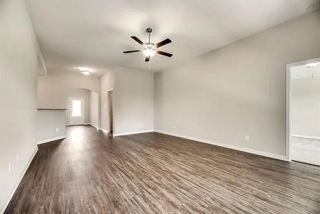 a view of an empty room with wooden floor and a ceiling fan