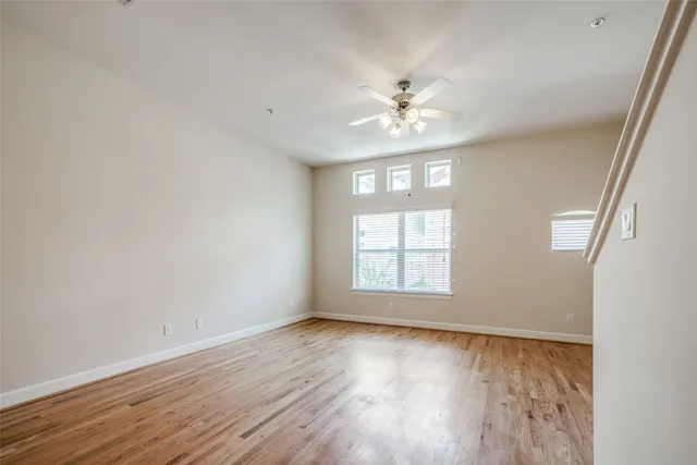 an empty room with wooden floor fan and windows