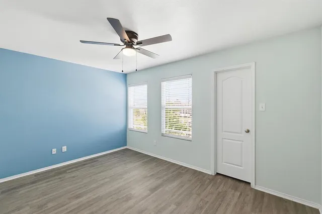 an empty room with wooden floor fan and windows