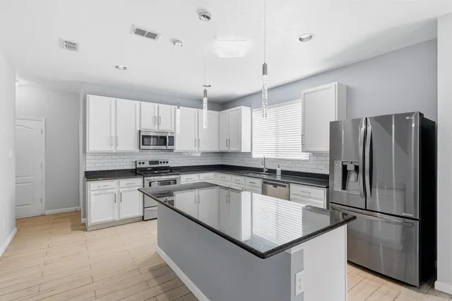 a kitchen with stainless steel appliances granite countertop a refrigerator a sink a stove a microwave and white cabinets