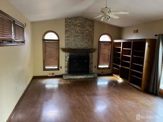 an empty room with wooden floor fireplace and windows
