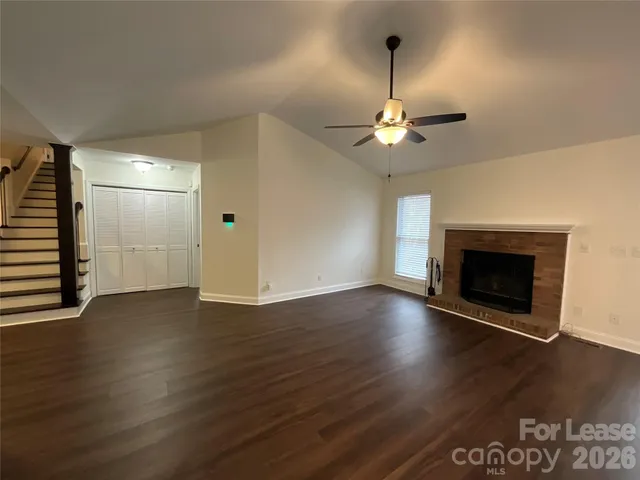 an empty room with wooden floor a chandelier fan and a fireplace