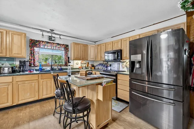 a kitchen with stainless steel appliances kitchen island granite countertop a table chairs in it and a wooden floor