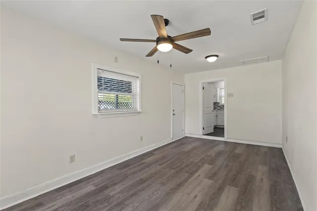 an empty room with wooden floor ceiling fan and windows
