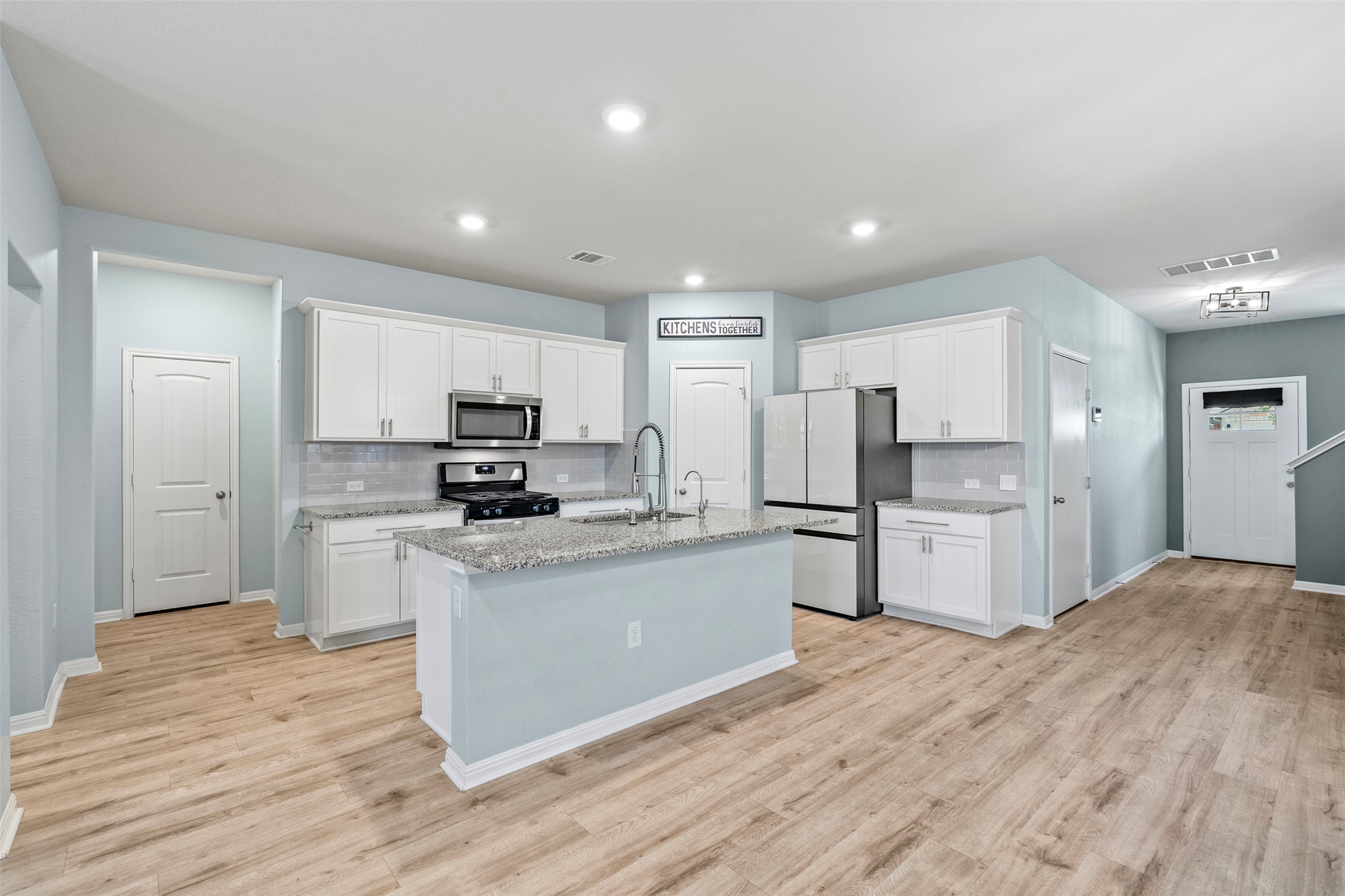 120 Ellinger Road Georgetown, TX 78626 - Photo 1 of 28 Open-concept kitchen featuring an island with a breakfast bar, white cabinetry, stainless steel appliances, and light-toned wood-finish flooring