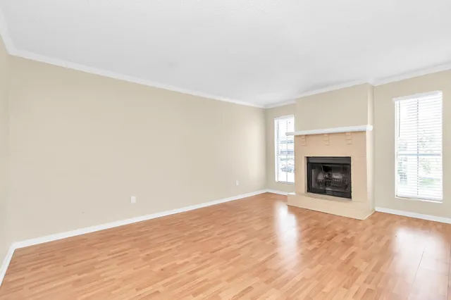 an empty room with wooden floor fireplace and windows