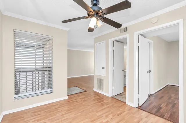a view of an empty room with wooden floor and a ceiling fan