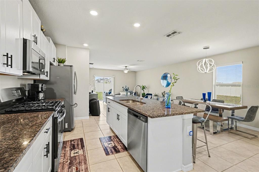 9424 Lemon Drop Loop Sun City Center, FL 33573 - Photo 5 of 31 a open kitchen with stainless steel appliances granite countertop a stove top oven a sink a dining table and chairs with wooden floor