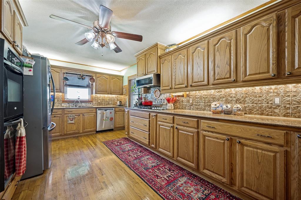 117 County Road Decatur, TX 76234 - Photo 9 of 40 Extensive wood cabinetry, patterned tile backsplash, wood-finish flooring, and a ceiling fan with integrated lighting
