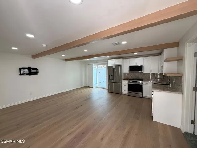 an empty room with wooden floor and kitchen view