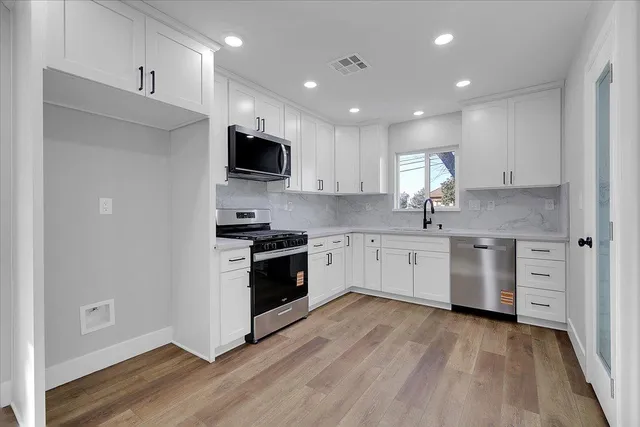 a kitchen with stainless steel appliances white cabinets a sink a stove a microwave and wooden floors