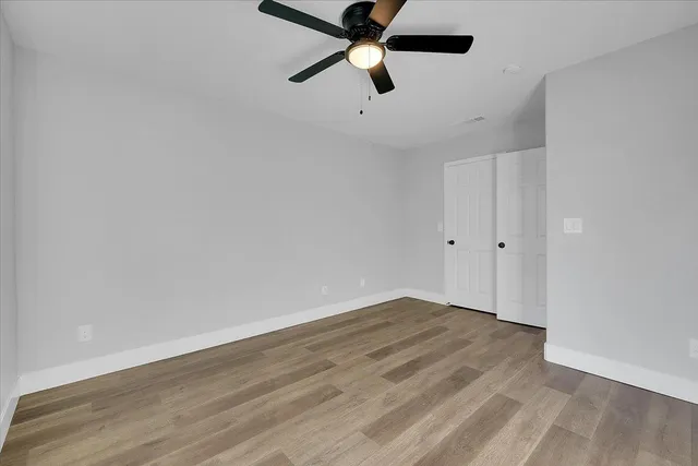 an empty room with wooden floor ceiling fan and window