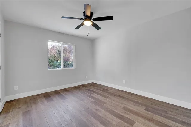 an empty room with wooden floor ceiling fan and windows