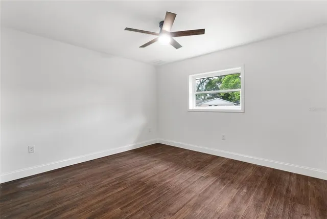 a view of an empty room with wooden floor and a ceiling fan