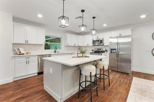 a kitchen with stainless steel appliances kitchen island granite countertop a sink a stove a refrigerator and island with wooden floor