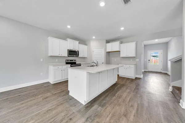 a large kitchen with stainless steel appliances granite countertop a stove a sink a refrigerator and white cabinets with wooden floor