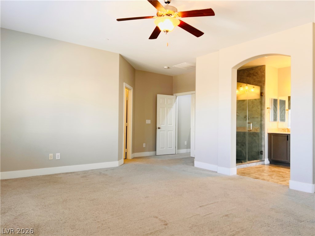 161 Dunblane Street Henderson, NV 89012 - Photo 47 of 56 A spacious primary bedroom features carpeted flooring and a ceiling fan, with an arched entryway leading to the primary bathroom.