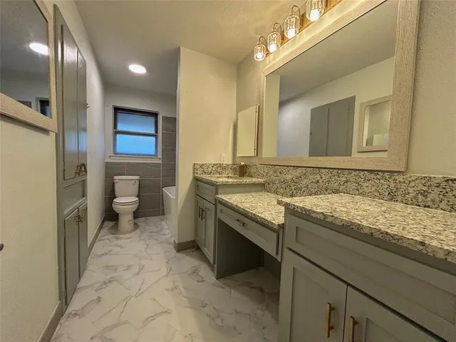 a bathroom with a granite countertop sink a toilet and a mirror