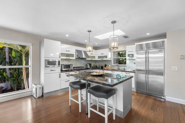 a kitchen with stainless steel appliances granite countertop a stove top oven a refrigerator a sink and chairs