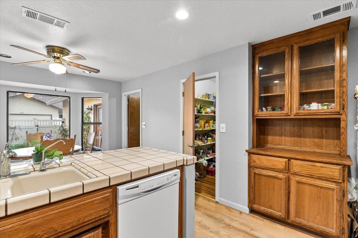 2136 Candy Cane Walk Manteca, CA 95336 - Photo 23 of 60 kitchen with glass insert cabinets, wood finish cabinets, tile countertops, a ceiling fan, and white dishwasher