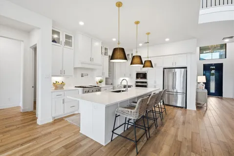 a kitchen with stainless steel appliances a stove a sink a refrigerator and a dining table with wooden floor