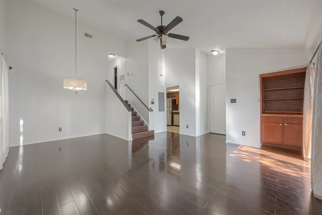a view of an empty room with wooden floor and a ceiling fan