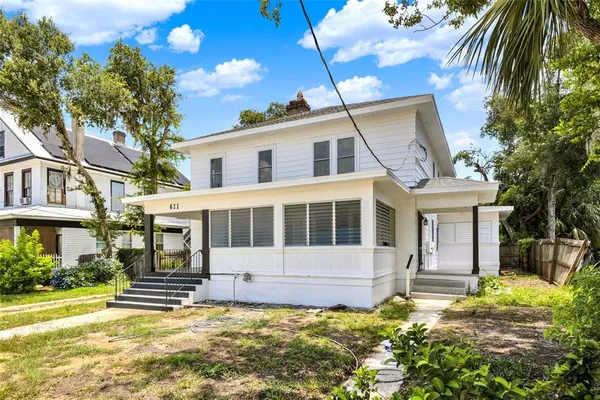 a view of a white house with a large windows and a yard with plants and large trees