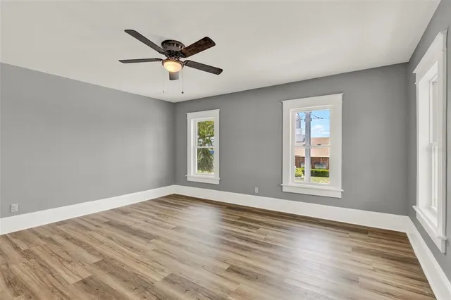 an empty room with wooden floor fan and windows
