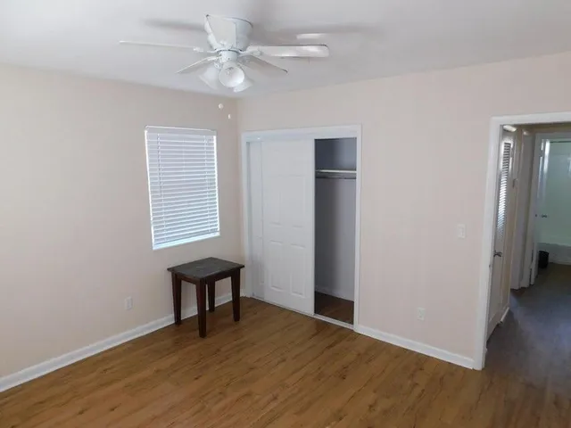 an empty room with wooden floor fan and windows