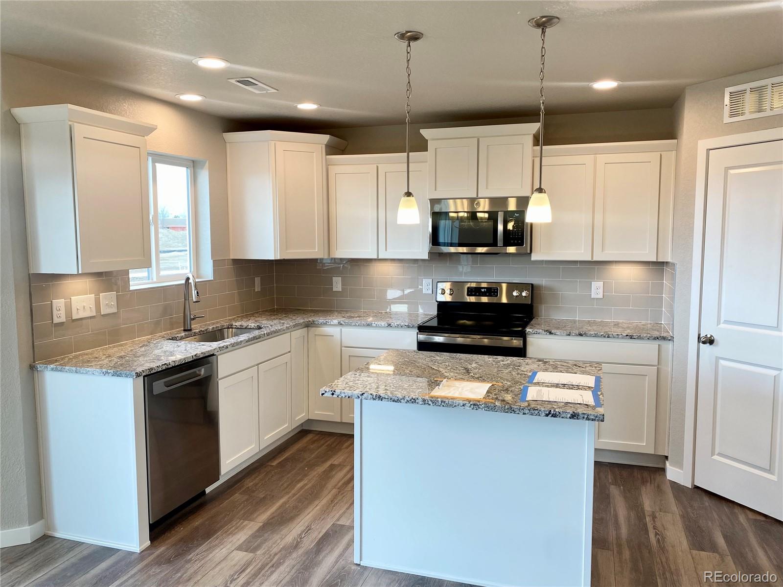 541 Ryan Avenue Fort Lupton, CO 80621 - Photo 4 of 29 a kitchen with kitchen island granite countertop a sink cabinets and wooden floor