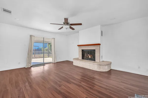 a view of an empty room with wooden floor fireplace and a window