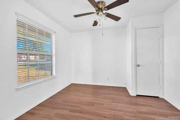 an empty room with wooden floor fan and windows