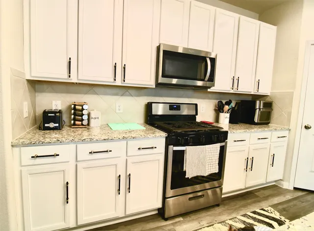 a kitchen with stainless steel appliances granite countertop grey cabinets a stove a sink and dishwasher