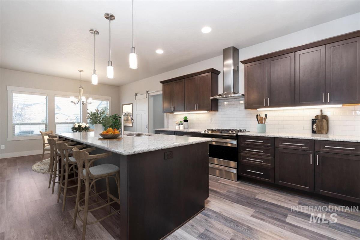 9580 West Ringle Creek Street Star, ID 83669 - Photo 13 of 43 Kitchen with dark wood finish cabinets, stainless steel gas stove, light stone counters, a barn door, and a kitchen bar