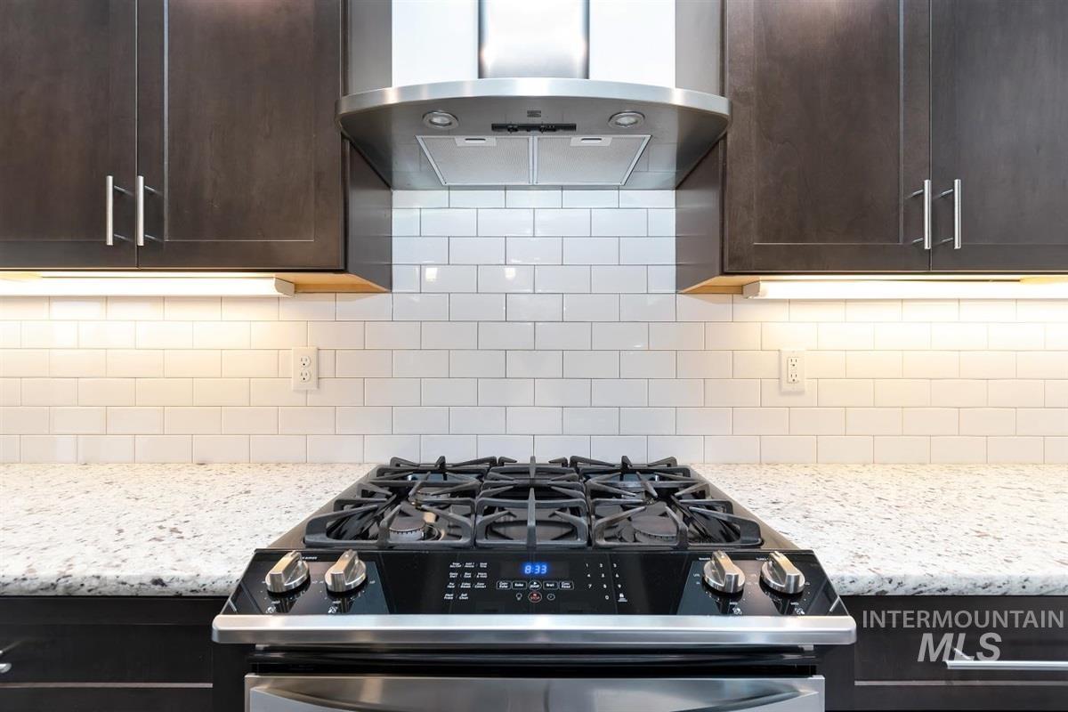 9580 West Ringle Creek Street Star, ID 83669 - Photo 16 of 43 Kitchen with ventilation hood, gas range, dark wood finish cabinetry, light stone countertops, and backsplash